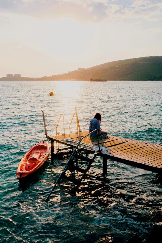 Person resting on a dock at sunset beside a kayak